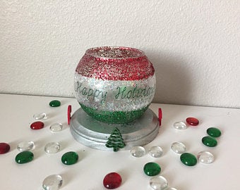 Base is crafted from pine wood and painted in metallic silver.  Overall measures 5 inches in diameter x 4 inches high.  Glass holder is decorated in red, silver & green glitter. "Happy Holidays" saying and Christmas embellishments are added for a final touch.
