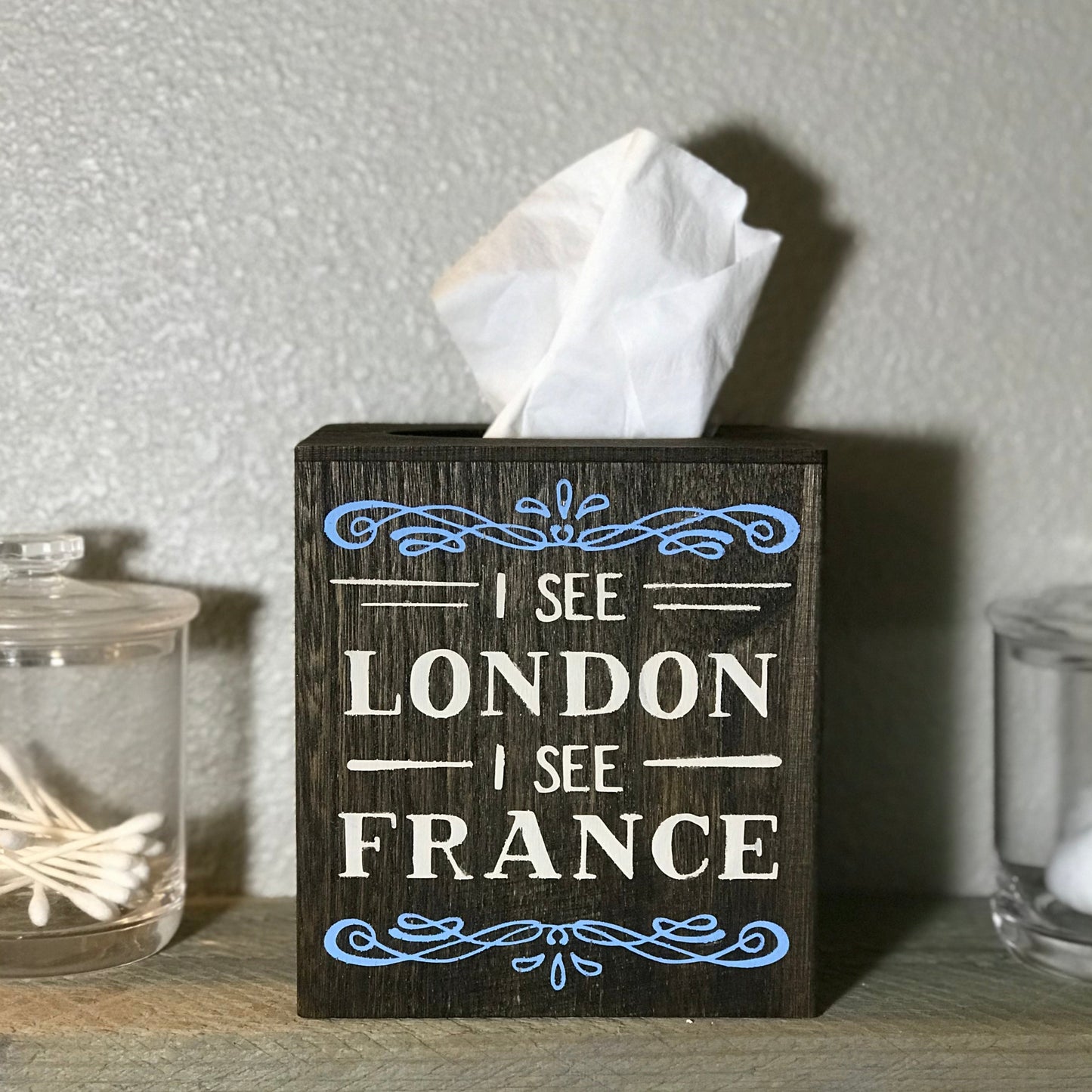 Crafted from wood. Measures 5.75 inch x 5.25 inch and will fit any standard size facial tissue box (not included). The box is stained in brown.  Saying "I See London I See France" painted on in cream with blue accents. The saying is on one side only.